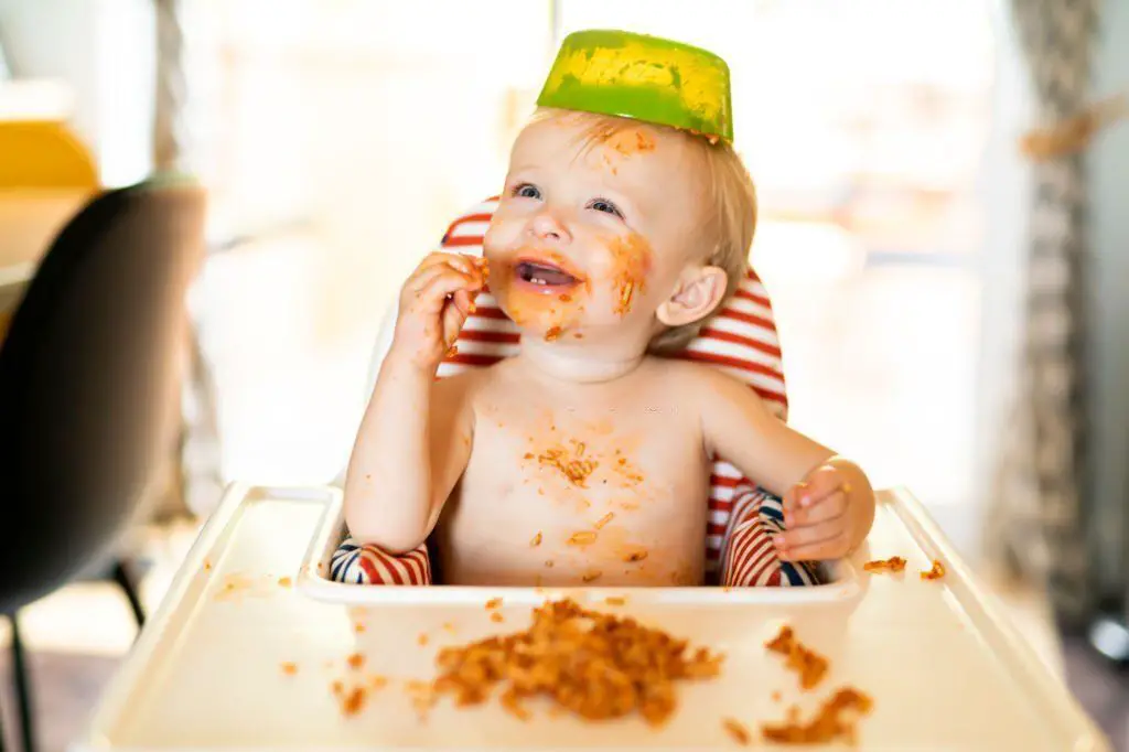 Bebé comiendo solo con plato puesto a modo de gorro